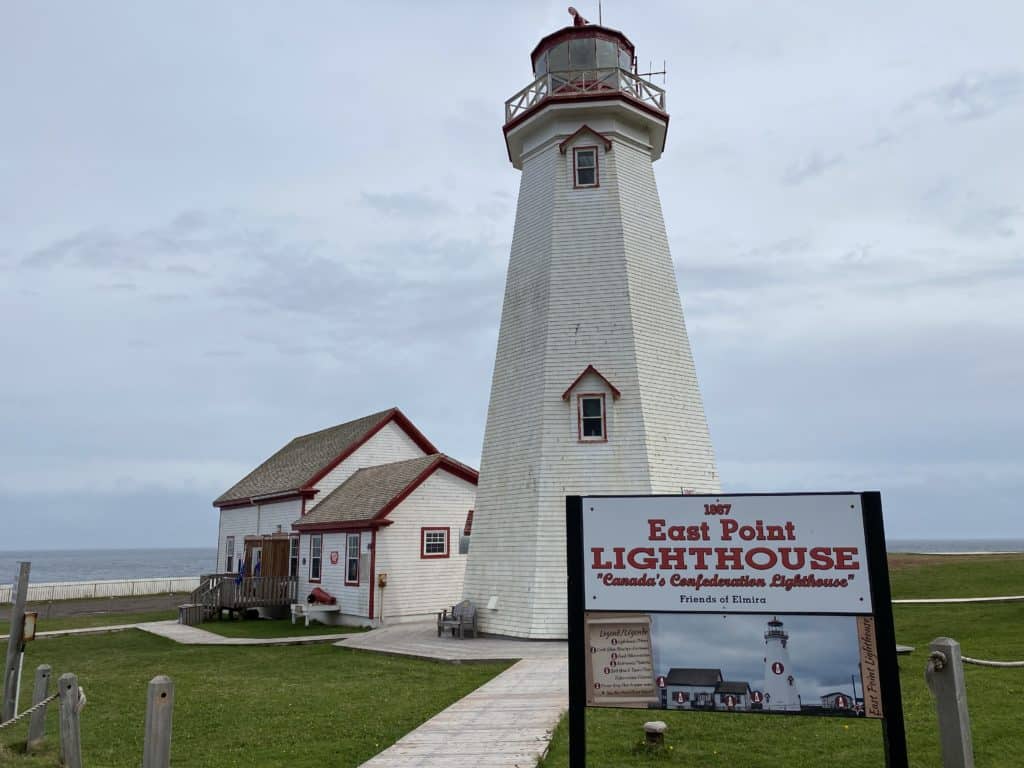 East Point Lighthouse and Keeper's house with sign facing ocean in background.
