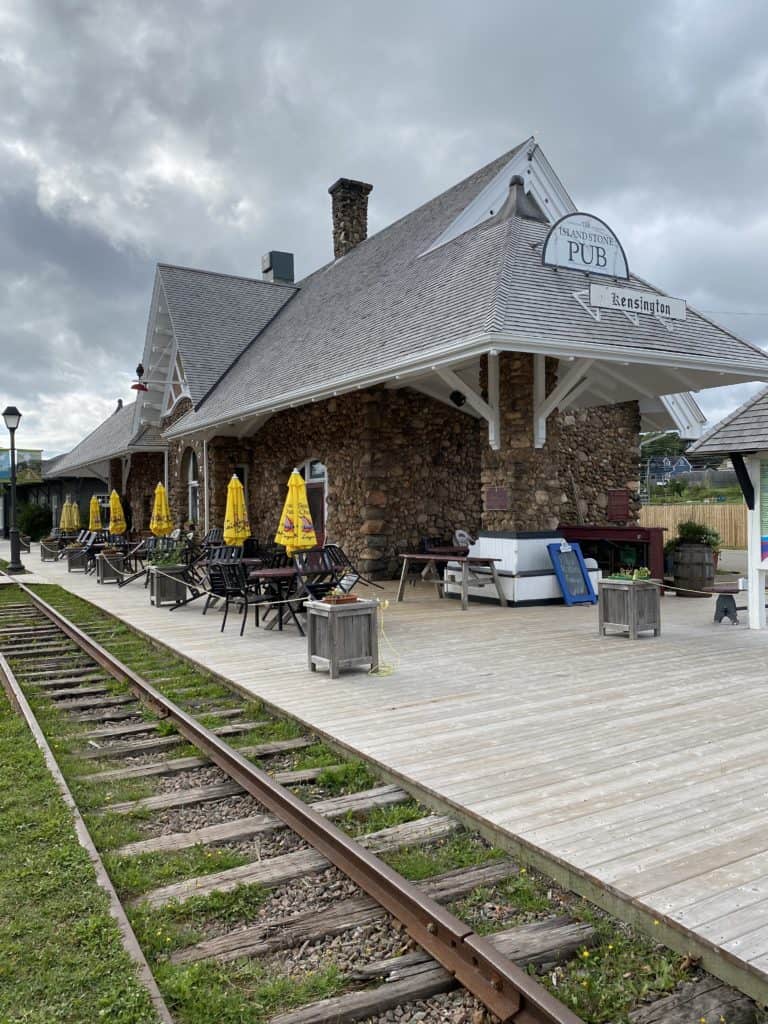train tracks alongside train station and wooden platform with tables, chairs and yellow umbrellas