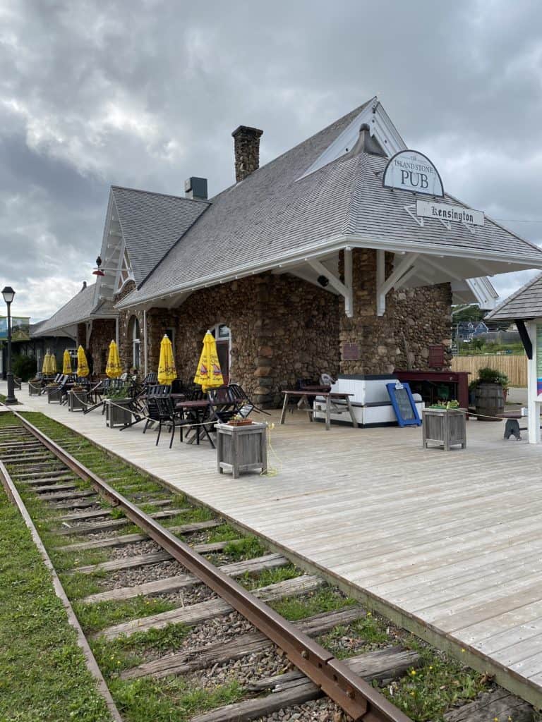 Train tracks alongside Kensington train station and wooden platform with tables, chairs and yellow umbrellas.