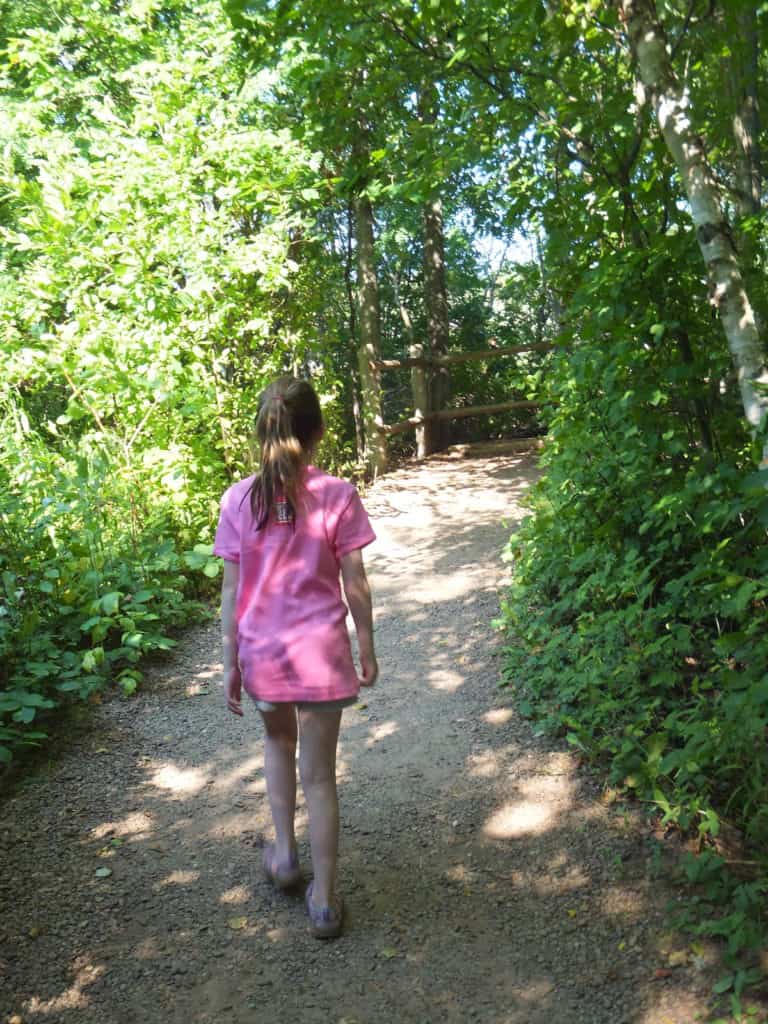 Young girl in pink shirt and shorts walking on path in woods.