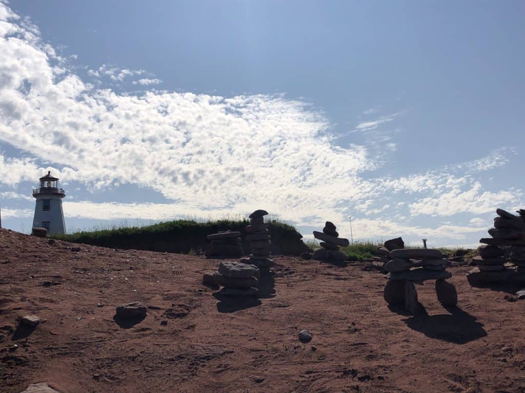 North Cape Lighthouse in background of red sand shore and inukshuks.
