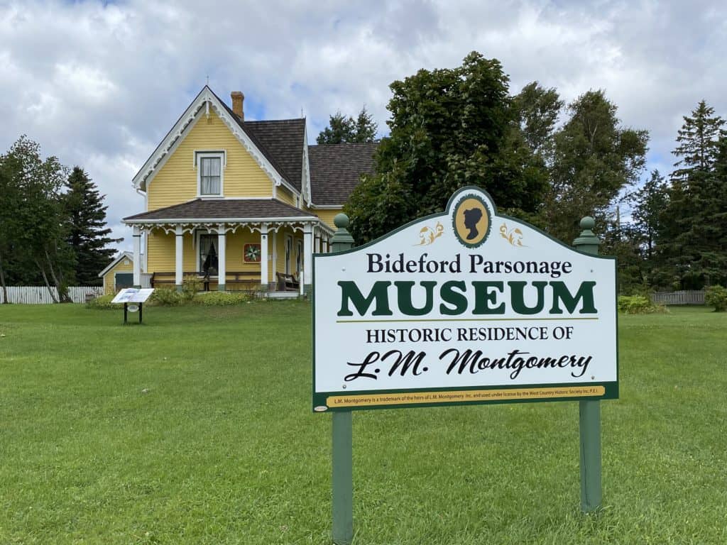 Yellow home with white trim and porch with sign identifying it as the Bideford Parsonage Museum - Historic Residence of L.M. Montgomery.