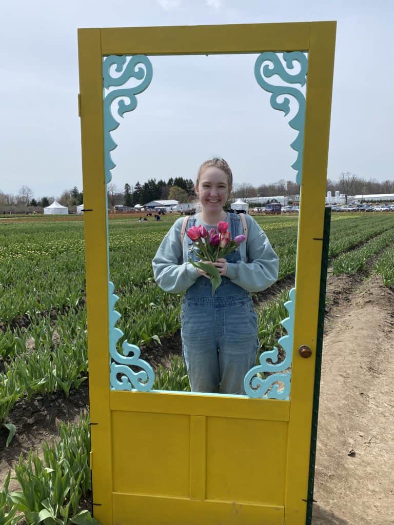 Young woman holding bouquet of tulips behind yellow doorframe at Tasc Tulip Farm.