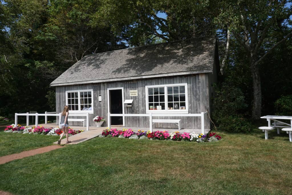 Young girl walking up path to small building with flower beds in front - bookstore on site of Lucy Maud Montgomery Cavendish home.