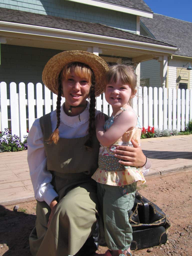 Young girl with Anne of Green Gables in front of white picket fence.