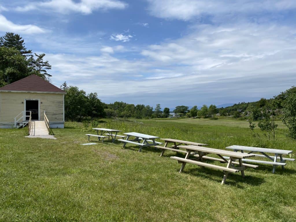 five picnic tables on grass outside old yellow building with ramp on Grosse-Île, Québec