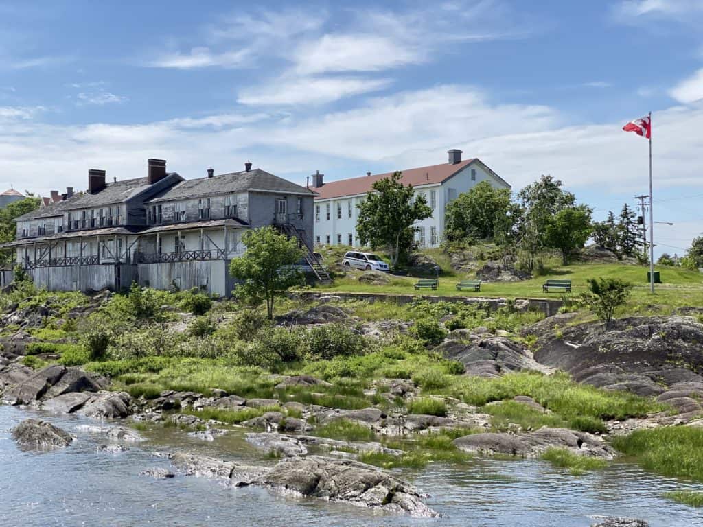 series of weathered grey buildings and one new white building along rocky coast of Grosse-Ile, Quebec