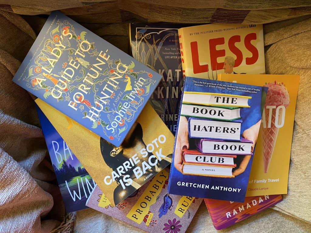 Flat lay of books sitting on top of a light brown blanket.