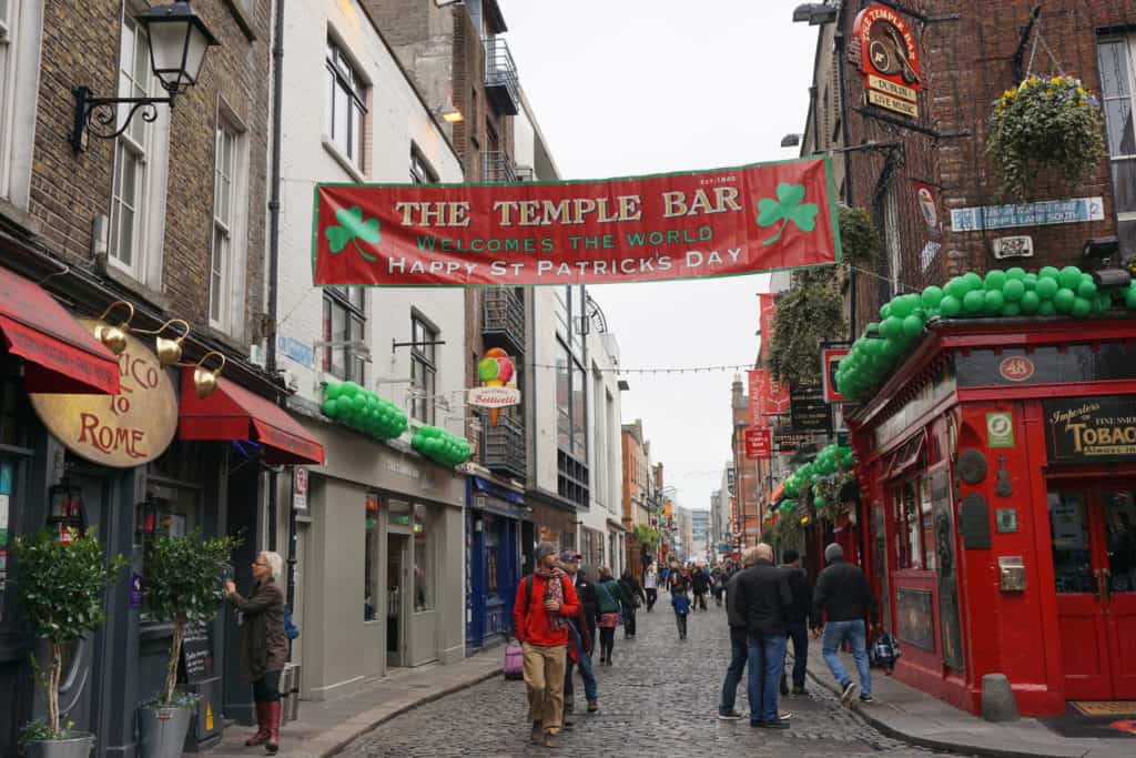 People walking in The Temple Bar neighbourhood of Dublin during St. Patrick's Festival with green balloon decorations.