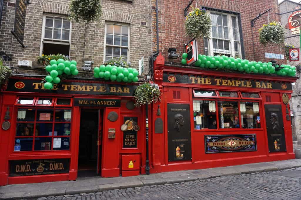 The Temple Bar in Dublin, Ireland decorated for St. Patrick's Day - red painted buildingon main level with green balloons above the words The Temple Bar.