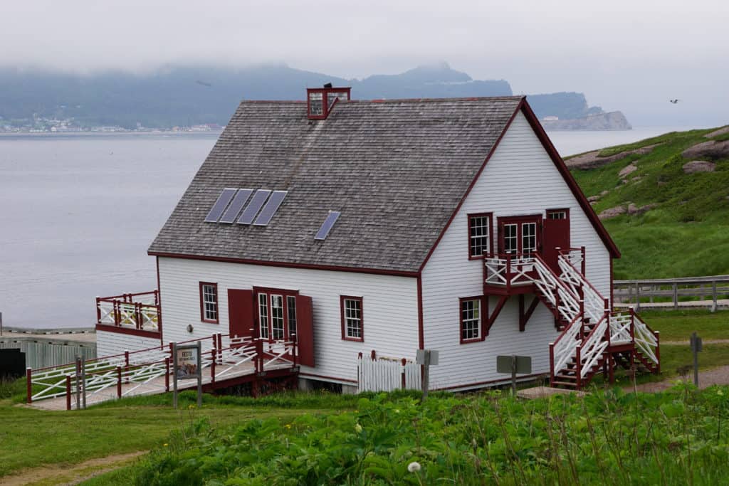 White building with red trim and grey shingled roof on Bonaventure island on foggy day.