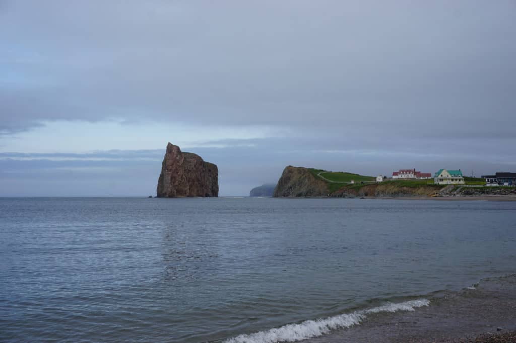 Perce Rock and buildings on mainland on overcast day.