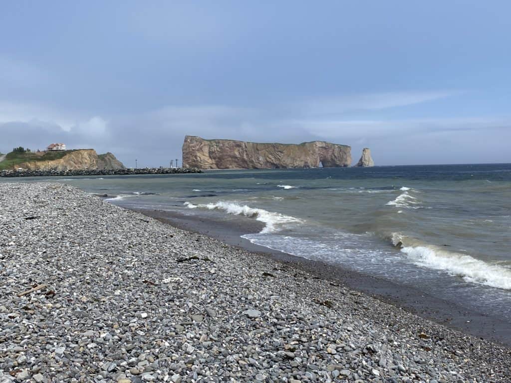 Stone beach and lapping waves with Perce Rock in distance.