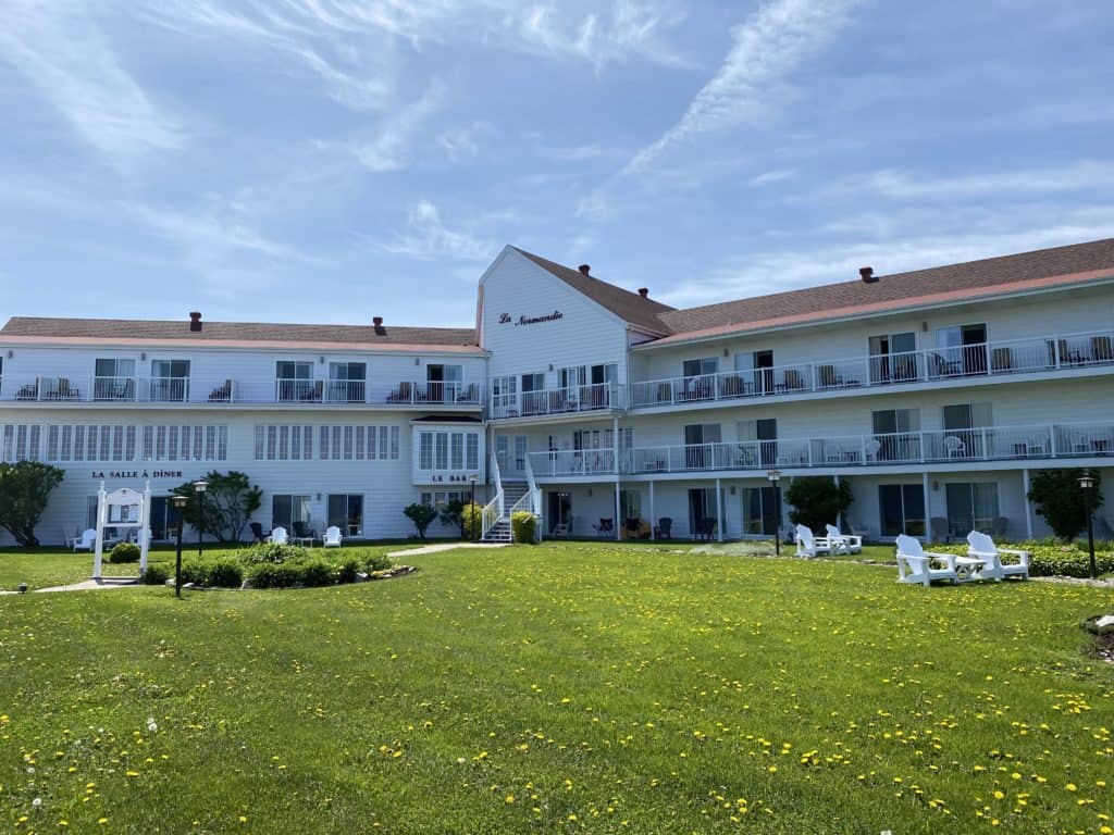 exterior of white beach hotel with red roof - green lawn and white chairs.