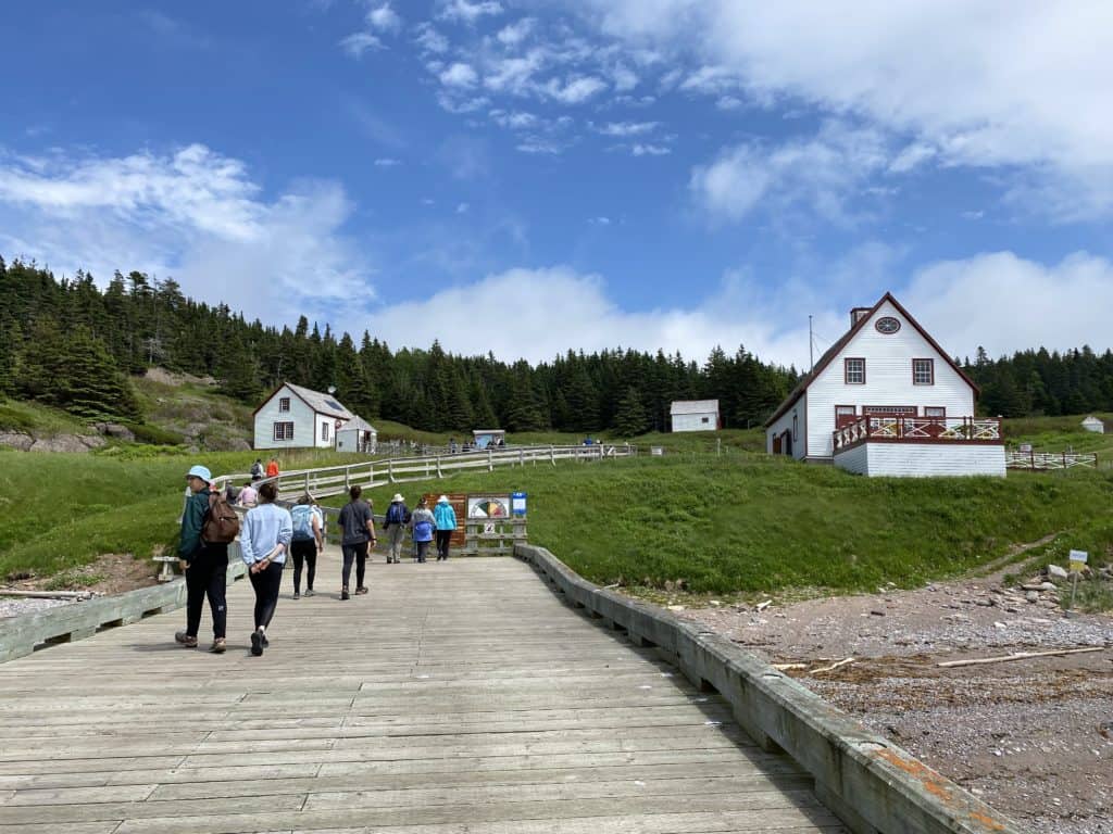 group of people walking on boardwalk toward white buildings with red trim - blue sky and white fluffy clouds