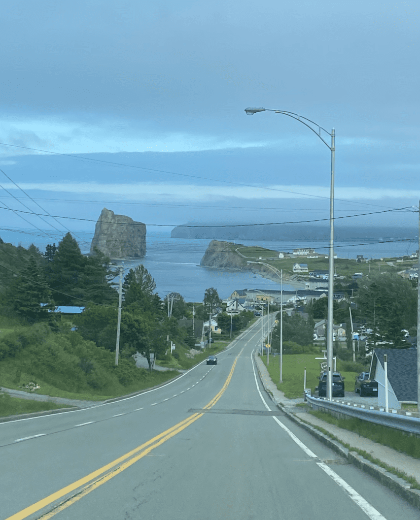Road leading into village of Perce with Perce Rock visible.