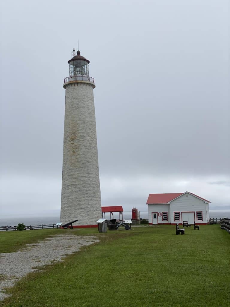 Cap-des-Rosiers lighthouse - tall grey tower tapering to top with white building red roof alongside on overcast day.