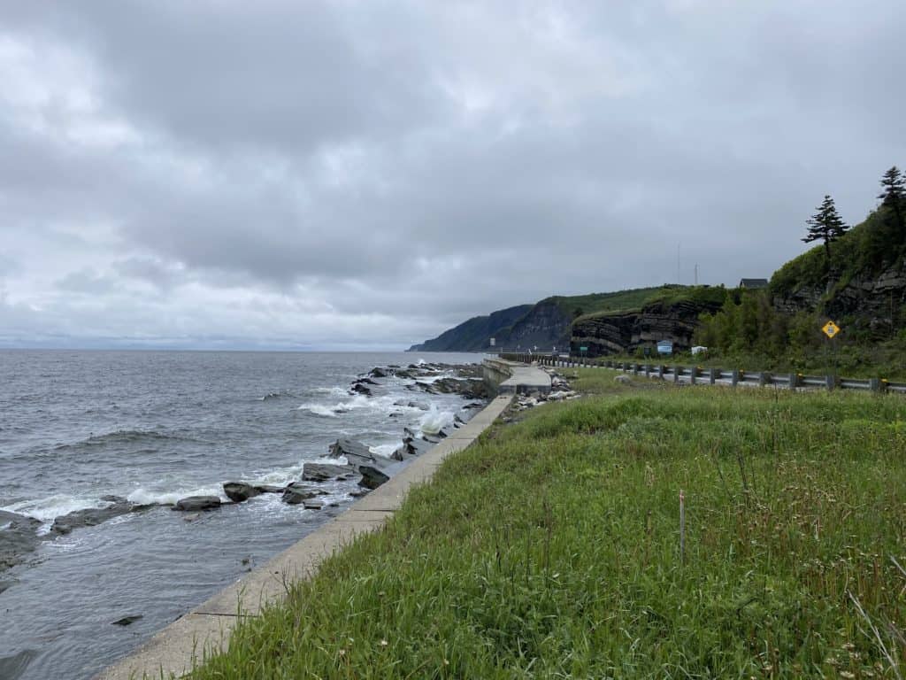 Roadside on Gaspe peninsula in Quebec with rocky coast on one side and hills on the other.