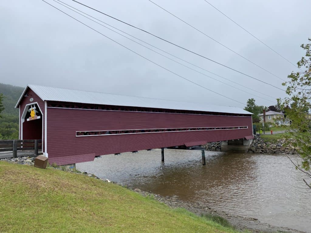 maroon coloured wooden covered bridge over river in Grand-Vallee, Quebec