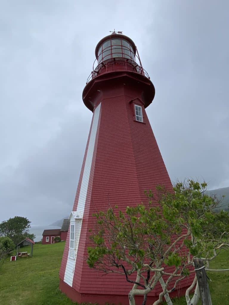 La Martre lighthouse - red with white stripe on front and small window beside small tree on overcast day.