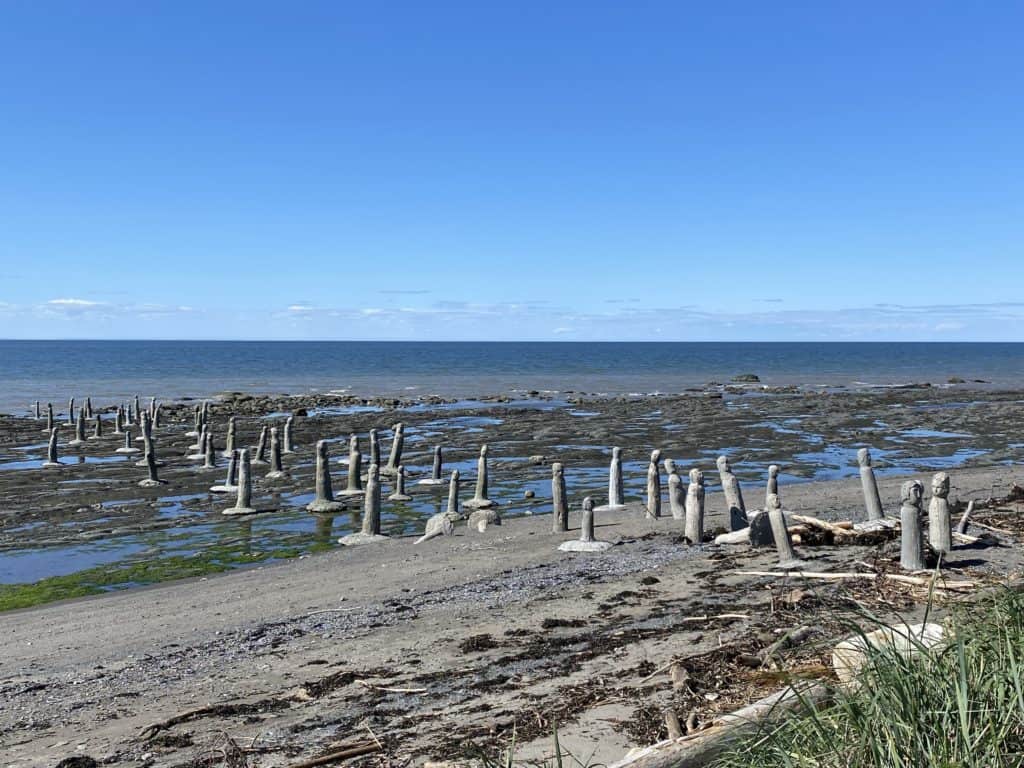 Le Grand Rassemblement - dozens of concrete human-like figures appearing to be walking out of the sea at low tide with bright blue sky.