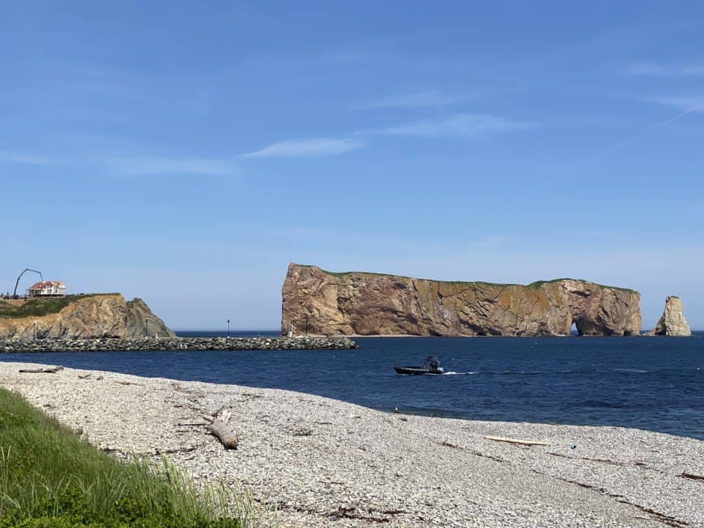 Perce Rock from rocky beach with small boat in foreground in Perce, Quebec.