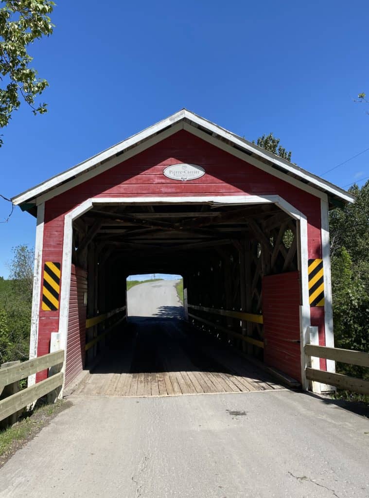 entrance to Pierre-Carrier red wooden covered bridge with bright blue sky in Sainte-Ulric, Quebec.