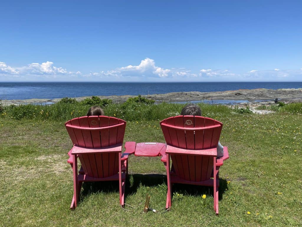 Two people sitting in red Parks Canada chairs looking at St. Lawrence River in Rimouski, Quebec.