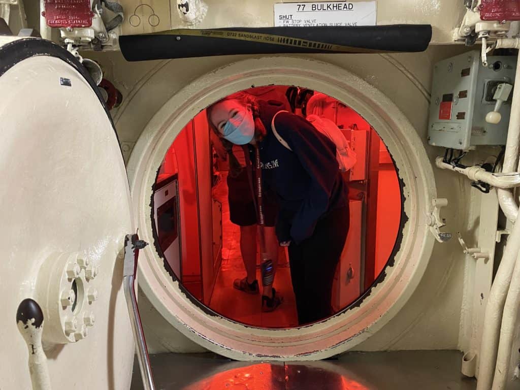 Young woman wearing face mask looking through passageway in Onondoga submarine, Point-au-Pere historic site, Rimouski, Quebec.