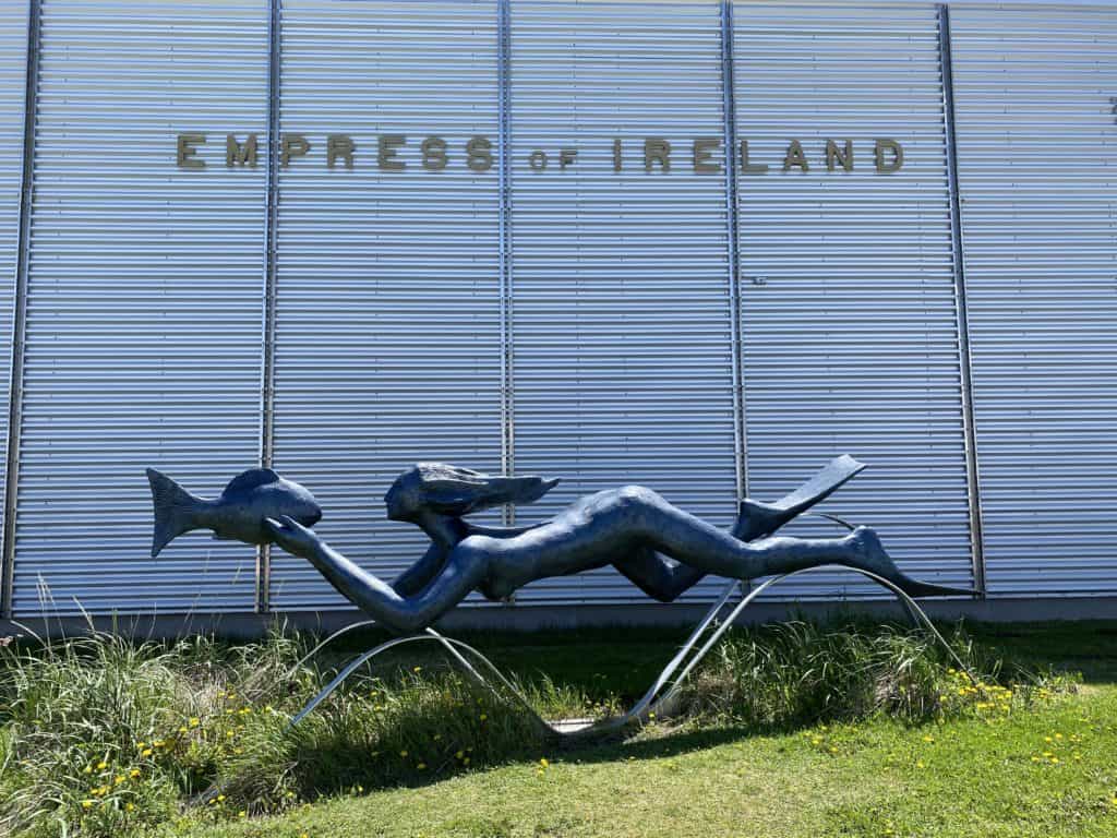Sculpture of woman swimming holding fish in front of wall of Empress of Ireland Museum, Rimouski, Quebec.