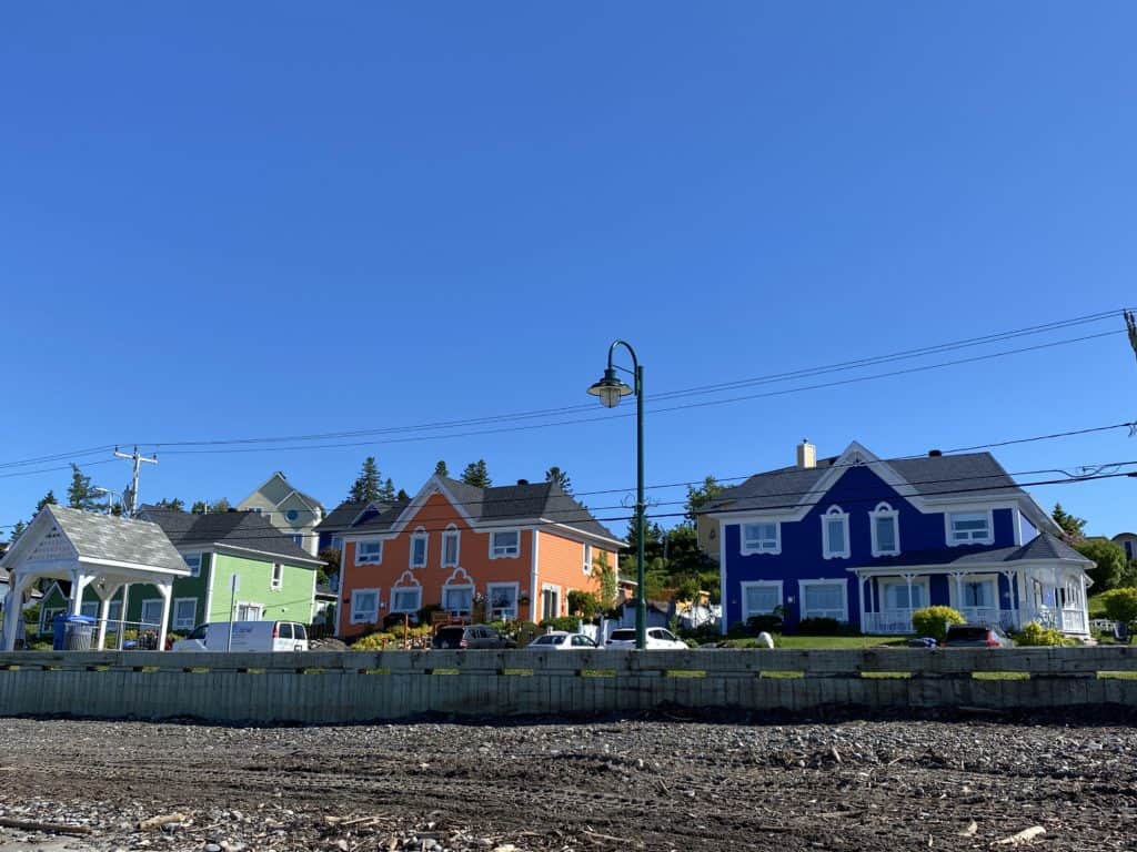 Green, orange, and blue houses with white trim near waterfront in Sainte-Luce, Quebec.