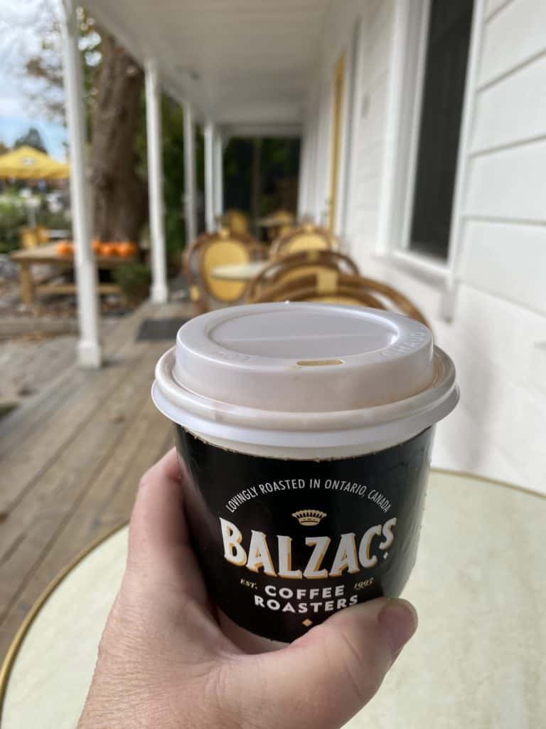 Hand holding cup of Balzac's coffee on porch of shop in Kleinburg.