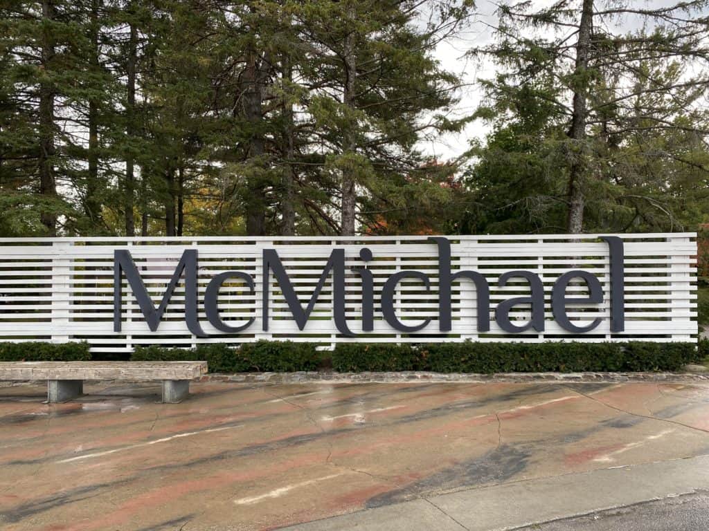 Sign reading McMichael in dark letters on white slats at McMichael Gallery.