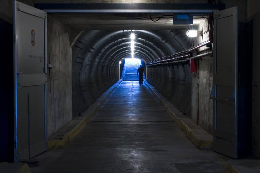 Man walking in dark underground tunnel with light opening at end.