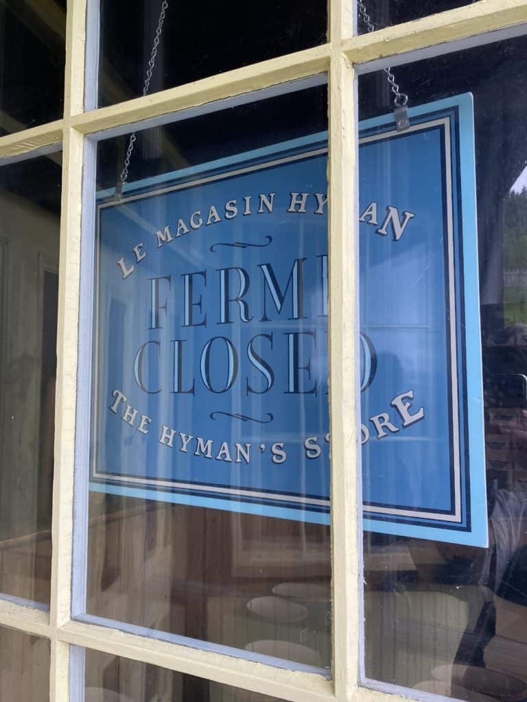 Bright blue sign hanging in panelled glass window says Le Magasin Hyman Ferme Closed The Hyman's Store.