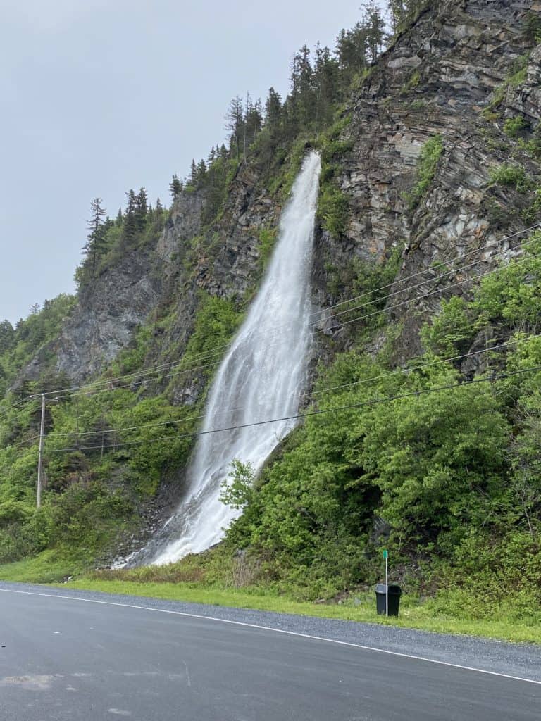 La Martre waterfall - water cascading down tree-covered cliff alongside highway with powerlines.