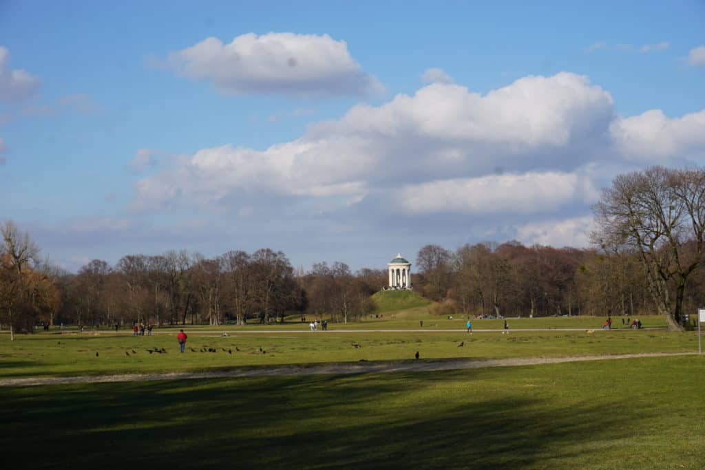 People enjoying the English Garden in Munich, Germany on a spring day - domed structure in background.