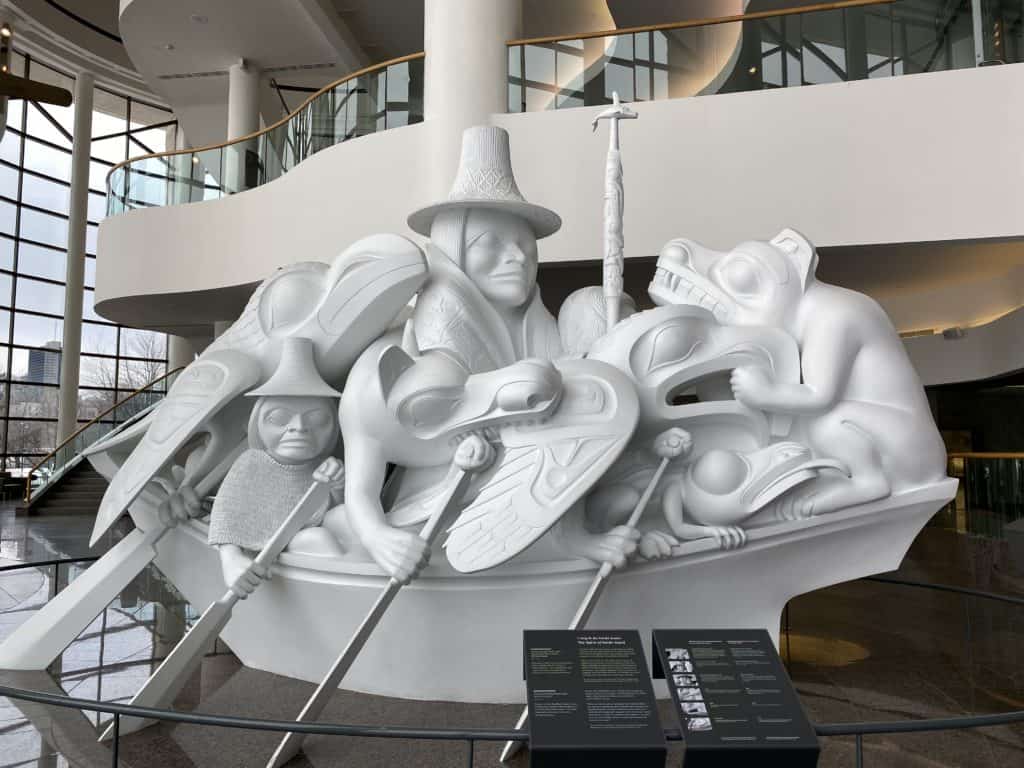 The Spirit of Haida Gwaii sculpture at the Canadian Museum of History in Ottawa. White sculpture of people and spirit animals paddling a canoe.