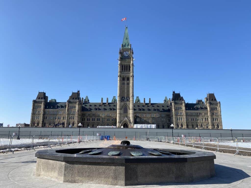 Bright blue sky and Centennial flame in front of Canadian Parliament buildings in Ottawa in winter.