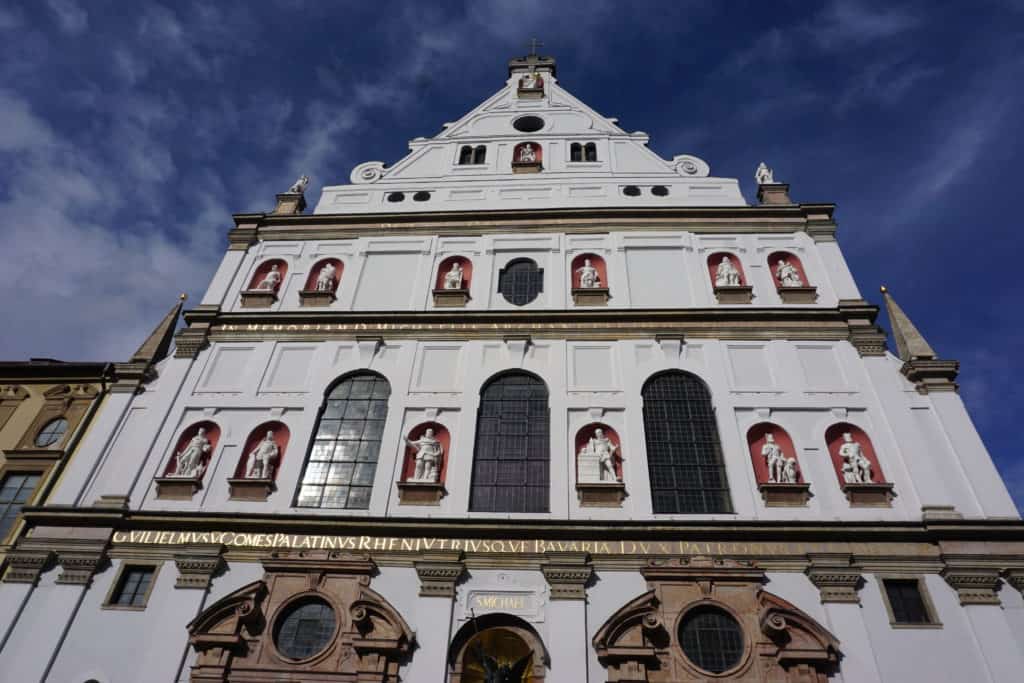 Extrerior of St. Michael's Church in Munich, Germany against bright blue sky. Mostly white exterior with figures inset.