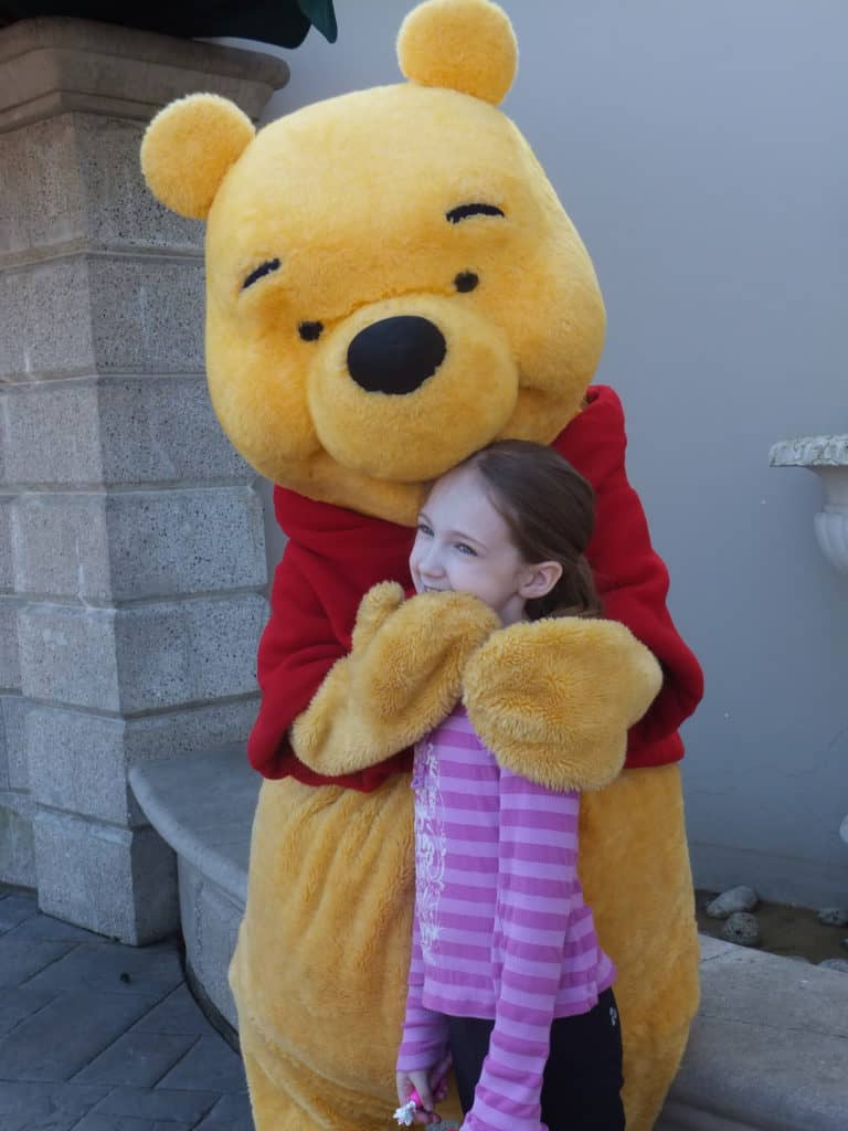 Young girl in purple shirt meeting Winnie-the-Pooh at Disneyland Paris.