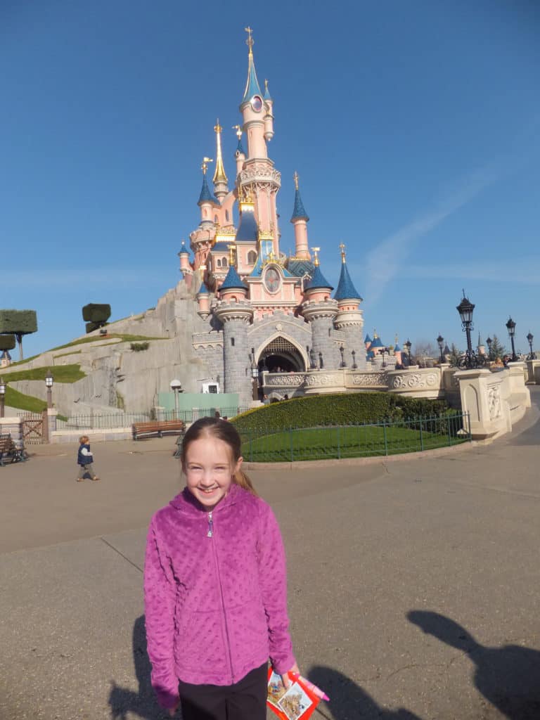Young girl in purple sweater in front of Sleeping Beauty's Castle at Disneyland Paris.