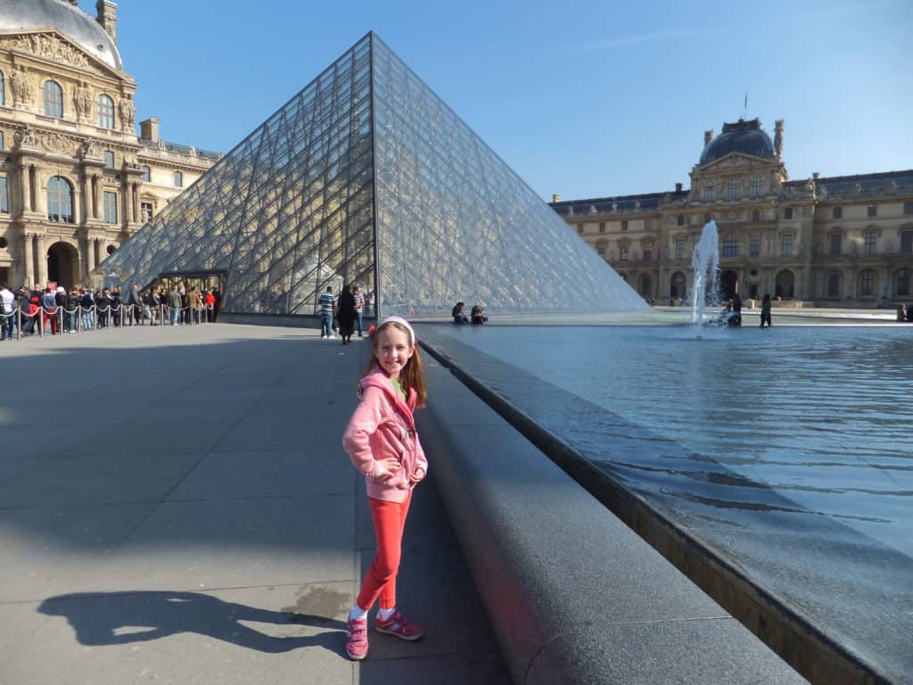 Young girl posing at the pyramid outside the Louvre Museum in Paris.