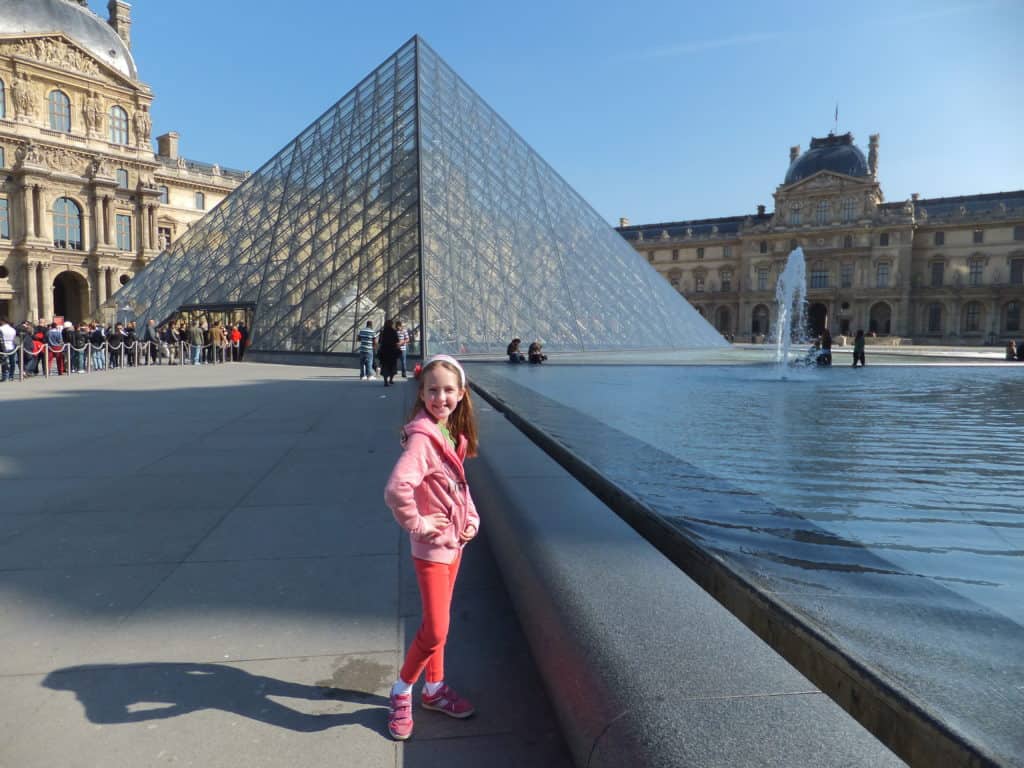 Young girl dressed in pink posing by the pyramid in front of the Louvre Museum in Paris, France.