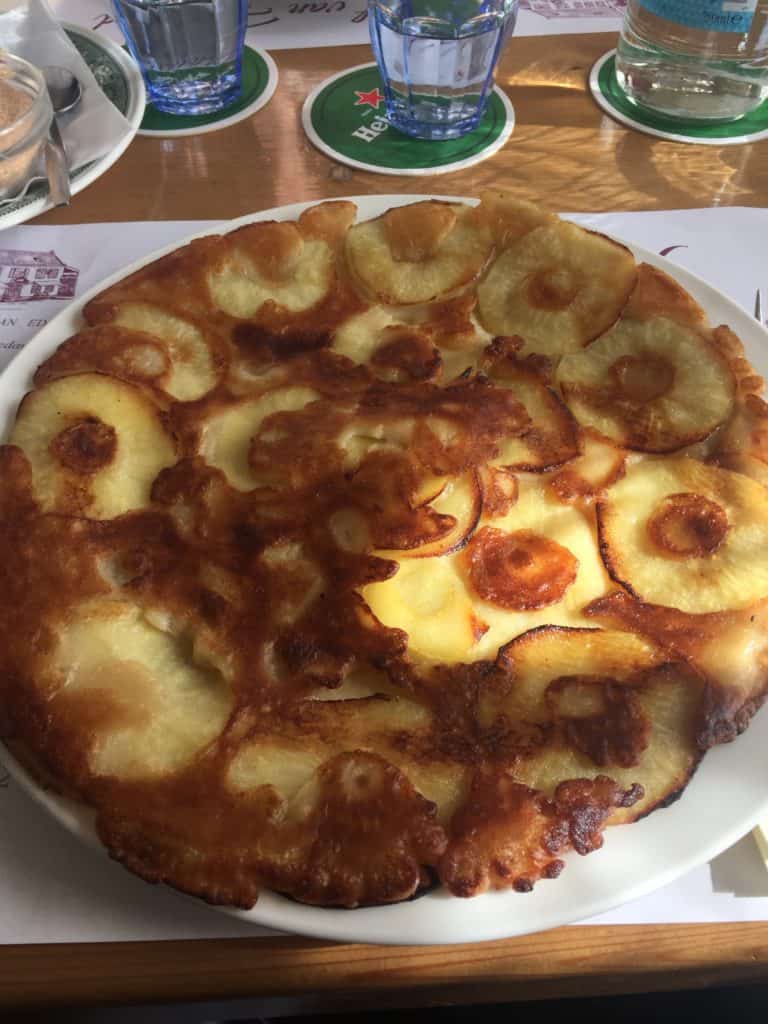Large Dutch pancake with apple slices on white plate.
