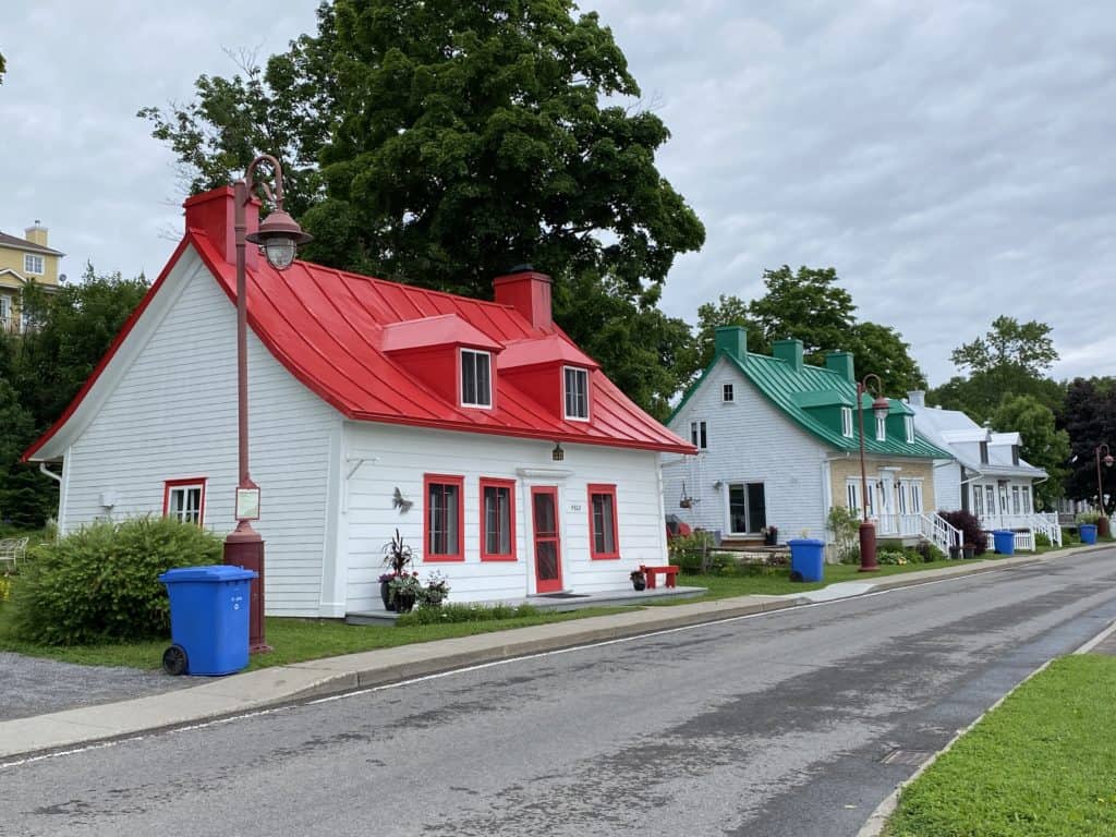 Row of three houses roadside in St. Jean on Île d'Orléans - white house with red roof in foreground, white ouse with green roof in middle, white house with white roof at end.