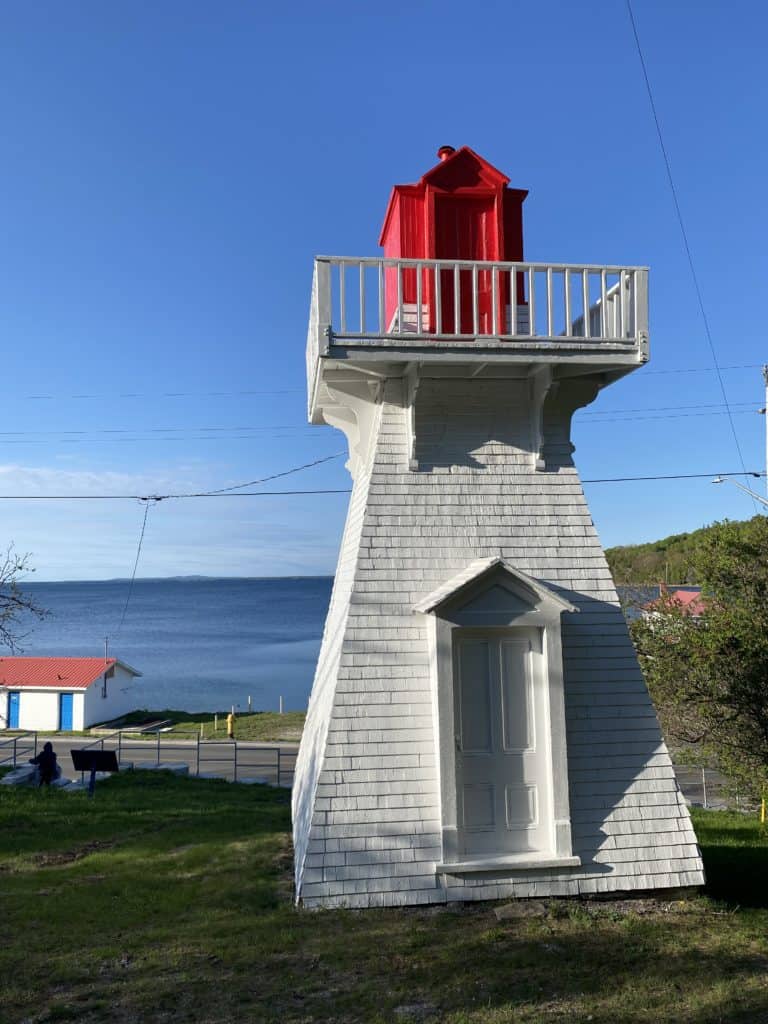 White wooden lighthouse with red light - Lake Huron and small building in background in Kagawong on Manitoulin Island.