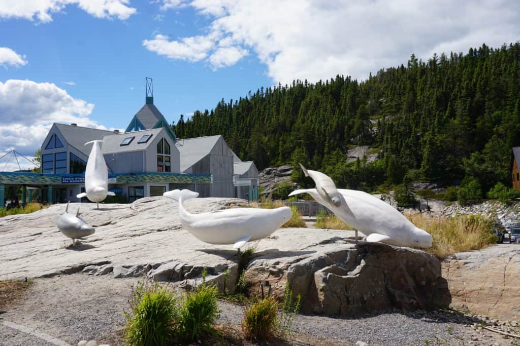 Marine Mammal Interpretation Centre in Tadoussac, Quebec in the background with large rock and sculpturees of whales in the foreground.