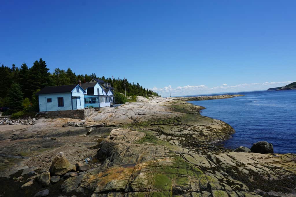 Light blue buildings with dark roofs on rocky shore in Tadoussac, Quebec.
