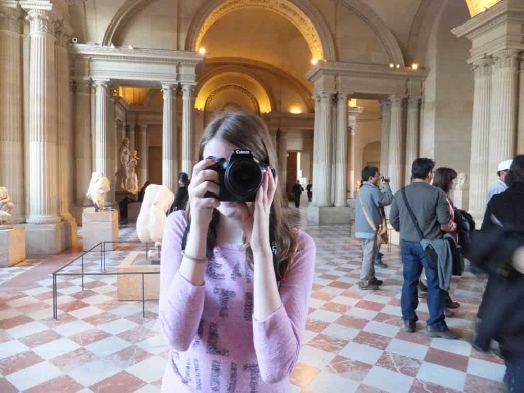 Teen girl in pink shirt taking photos in the Louvre in Paris.